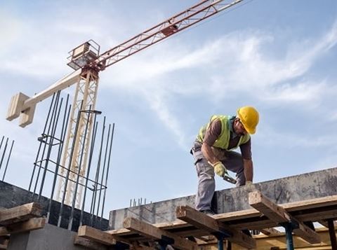 Man in PPE working on a construction site with a crane in the background.